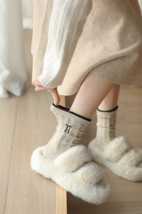Detail of beige wool socks with black bows and plush open-toe slippers on wooden floor