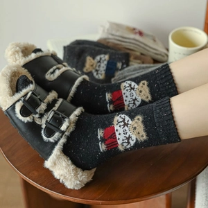 Detail of embroidered bear on black knit socks paired with fleece slippers