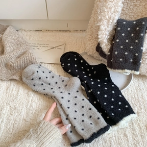 Chaussettes en peluche à pois gris et noirs disposées sur un tapis moelleux
