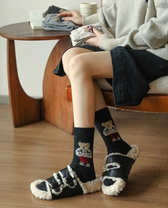 Detail of dark knit socks with white polka dots and teddy bear pattern worn with slippers