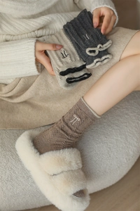 Detail of wool socks featuring bow embroidery and cable knit texture in warm colors