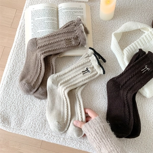 Macro detail of cable-knit wool socks featuring delicate bow embroidery in warm tones