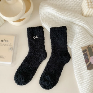 Dettaglio di calzini invernali in pile corallo nero con ricamo minimalista a forma di occhio