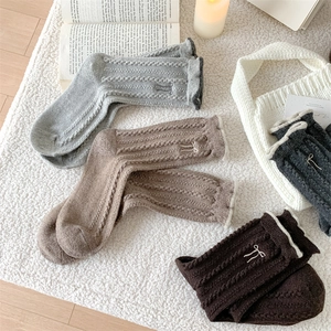Detail of wool cable knit socks featuring vintage bow embroidery and rolled cuffs