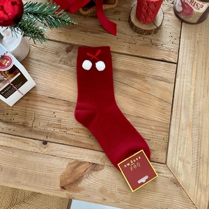 Close-up of red rabbit wool socks with white pom-poms and festive bow details