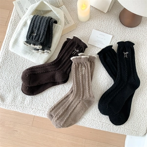 Detail of cable knit wool socks featuring ruffled edges and delicate bow embroidery