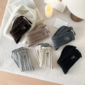 Detail of wool socks with cable knit texture and embroidered bow on cozy white rug