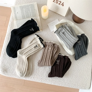Detail of wool socks with cable knit texture, ruffle cuffs, and bow embroidery