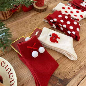 Close-up of festive red crew socks with white pom-poms, bow details and heart patterns