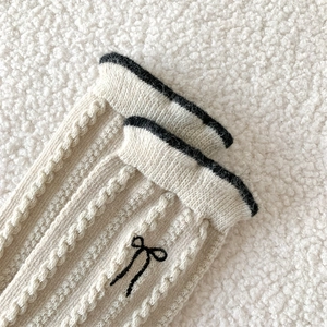 Close-up of cable knit wool socks with black bow embroidery and contrasting trim detail