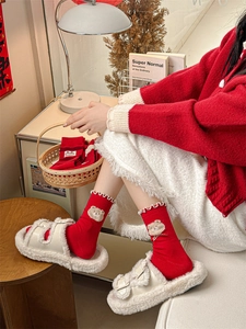 Detail of red crew socks with white lace trim and teddy bear embroidery with plush slippers