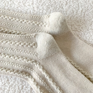 Detailed close-up of beige cable knit wool socks featuring intricate warm texture