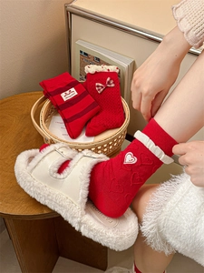 Detail of red festive socks with bow and heart embroidery next to white faux fur slippers