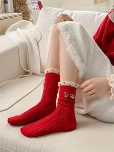 Close-up of red cable knit socks with cute plaid bows and white lace trim detail