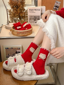 Detail of red knit mid-calf socks with plush bear, plaid bow and white ruffle trim