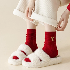 Close-up of red cotton socks with gold bow embroidery and white plush slippers