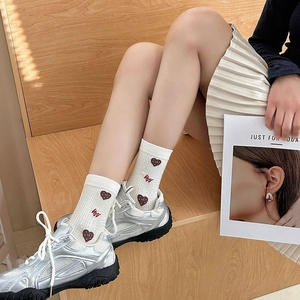 Detail view of cream cotton socks with red heart embroidery and wavy pattern on a model