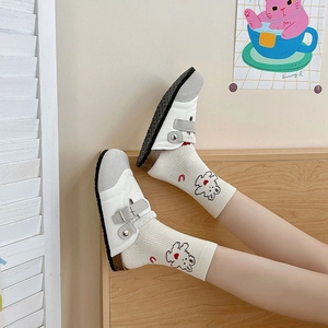 Close-up of white leather mule shoes with cartoon bear socks and red heart patterns