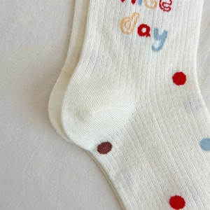 Detail of cream knit socks with colorful dots and 'Nice day' embroidery texture