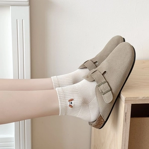 Side view of suede clog mules with metal buckle strap and cork footbed on a wooden floor