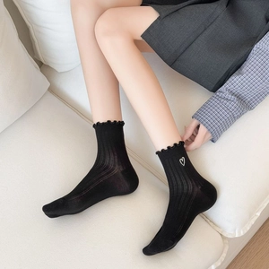 Detail of black cotton socks featuring ruffle edges and white heart embroidery