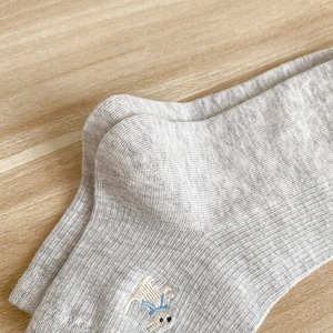 Dettaglio calzini in cotone a coste grigio chiaro con ricamo di cucciolo su legno