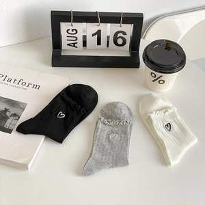 Trio of cotton socks in black, grey, and white with ruffle edges and heart embroidery