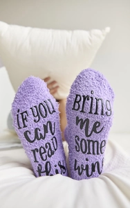 Close-up of purple fuzzy socks with black text bring me some wine printed on the soles
