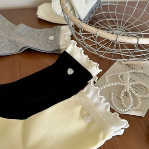 Détail du tricot de chaussettes mi-mollet avec volants et bouton en forme de cœur