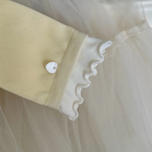 Détail de la manche en tricot jaune clair avec bord à volants et bouton cœur blanc