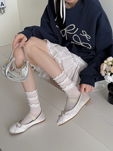 Detail of white satin ballet flats with bow and elastic strap worn with socks