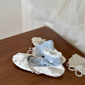 Détail de chaussettes bleues à volants avec boucle cœur et ballerines blanches sur bois