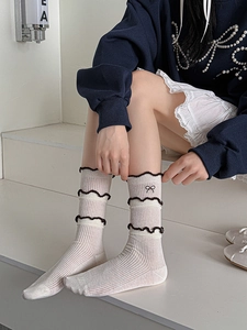 Detail of white ribbed cotton socks with scalloped lace trim and a cute black bow accent