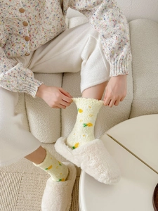 Close-up of yellow pineapple patterned socks paired with soft white plush home slippers