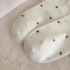 Detailed close-up of cream knit socks featuring black polka dot pattern and fine texture