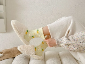Close-up of soft coral fleece socks with yellow pineapple pattern and plush white slippers