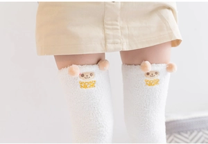 Détail de chaussettes hautes en polaire corail blanche avec broderie ours et pompons