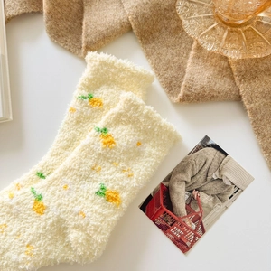 Detail of warm yellow coral fleece socks with pineapple pattern on white tabletop
