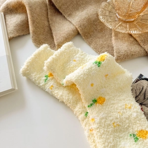 Close-up of thick beige coral fleece warm socks with yellow floral patterns on soft blanket