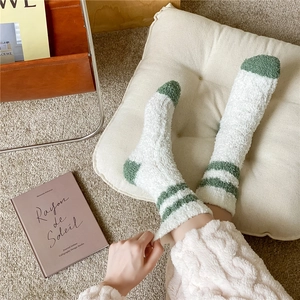 Detail of plush coral fleece socks with green stripes on a soft home carpet