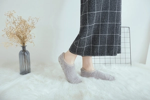 Detail of grey fluffy coral fleece socks with non-slip silicone dots on white rug
