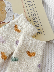 Close-up of thick coral fleece winter socks with colorful heart patterns on a soft knit background