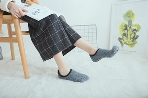 Detail of grey coral fleece floor socks with black piping worn in a cozy home setting