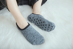 Detail of grey fluffy coral fleece socks with anti-slip silicone dots on white rug