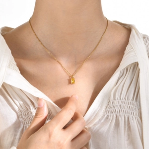 Detail of a gold necklace featuring a rectangular yellow zircon pendant on a model