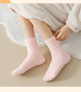 Detailed view of pink coral fleece socks with white non-slip grips on a plush carpet