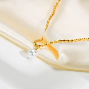 Detailed close-up of a golden bead necklace featuring a round white pearl on cream silk