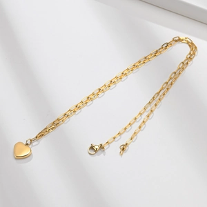 Détail du collier cœur doré avec chaîne trombone sur un fond blanc au style minimaliste