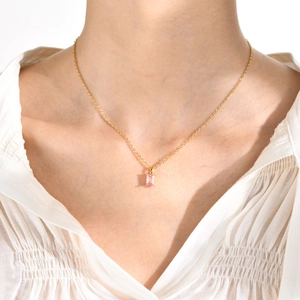 Detail of a gold necklace featuring a rectangular pink zircon pendant on a female model