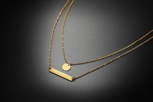 Detail of double-layer gold necklace featuring a round disc and flat bar pendant